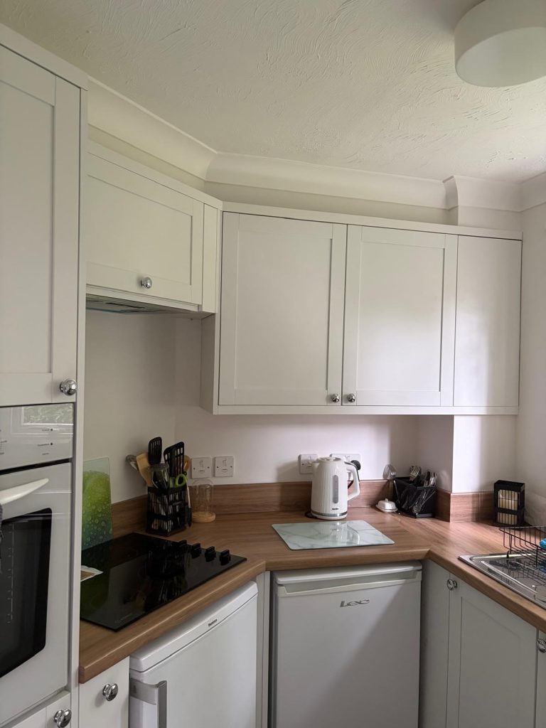 Newly completed kitchen featuring cream shaker-style wall and base cabinets, integrated oven and hob, wood-effect worktops, under-counter fridge, and contemporary chrome hardware in a space-efficient design.