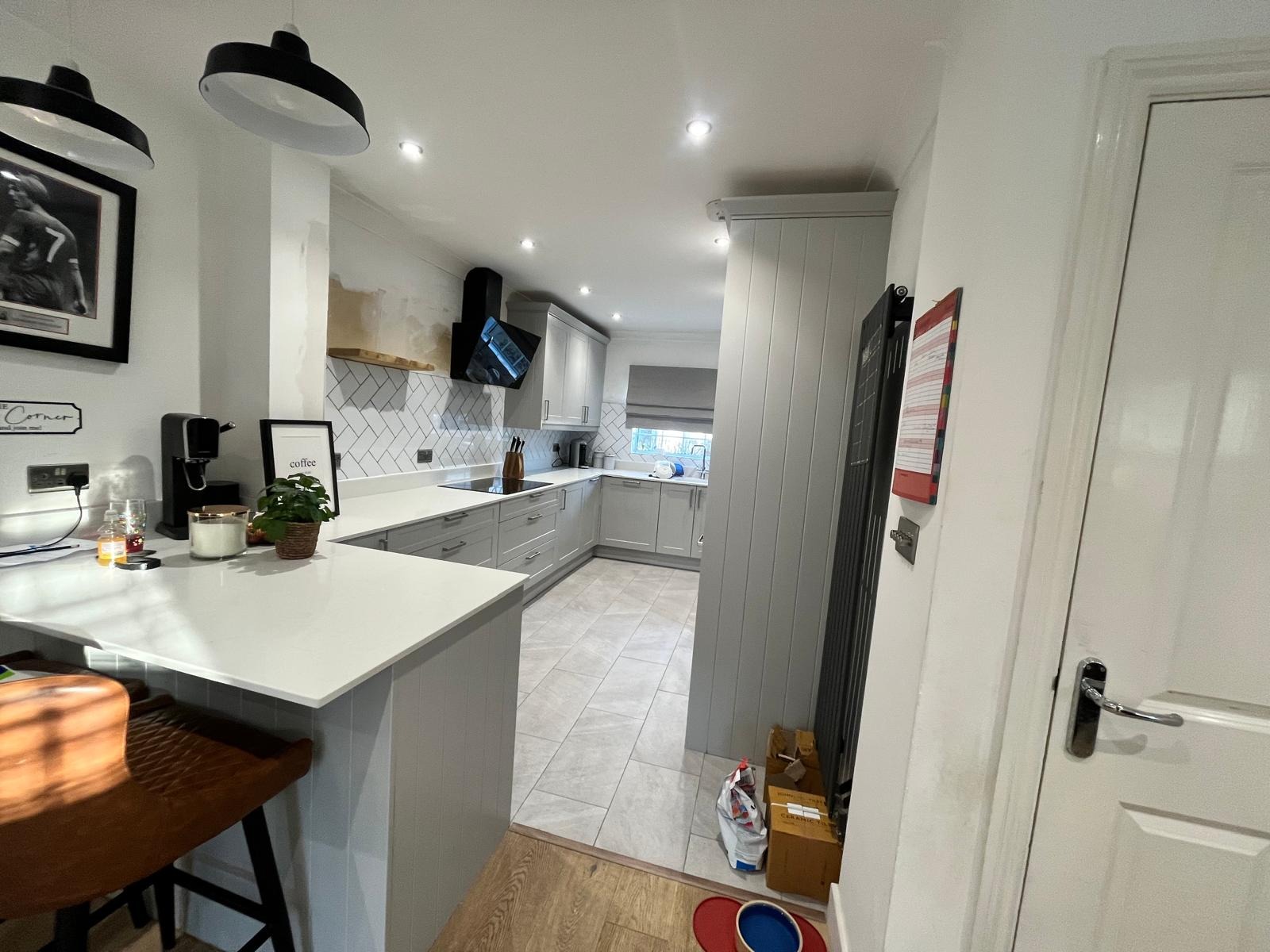 View from the breakfast bar of a completed Fleet kitchen showing white stone countertops, grey cabinetry, pendant lighting and new tiled flooring leading to the cooking area