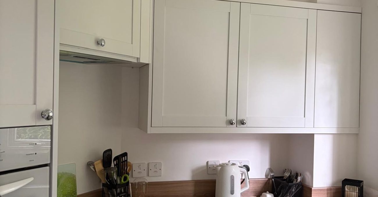 Newly completed kitchen featuring cream shaker-style wall and base cabinets, integrated oven and hob, wood-effect worktops, under-counter fridge, and contemporary chrome hardware in a space-efficient design.