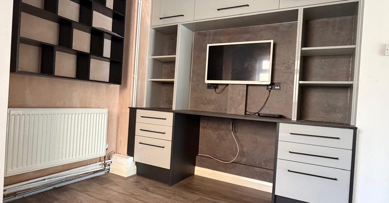 Bespoke fitted home office with grey cabinetry, black worktop, open shelving, wall-mounted TV and matching geometric wall storage.