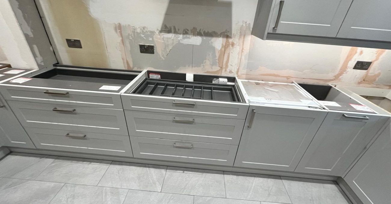 Before renovation view of a kitchen in Fleet with grey shaker-style cabinets, exposed wall plaster and a wall-mounted extractor hood ready for replacement