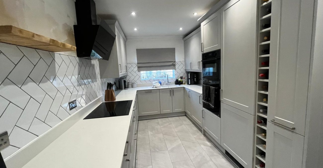 Full-length view of a completed Fleet kitchen with grey Neves cabinetry, herringbone splashback tiles, stone worktops, black oven and wine storage unit