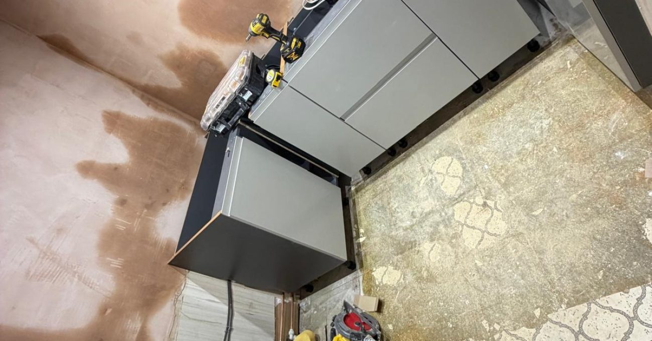 Newly installed grey base cabinets on castors with bare plastered walls, showing mid-installation progress of the kitchen renovation