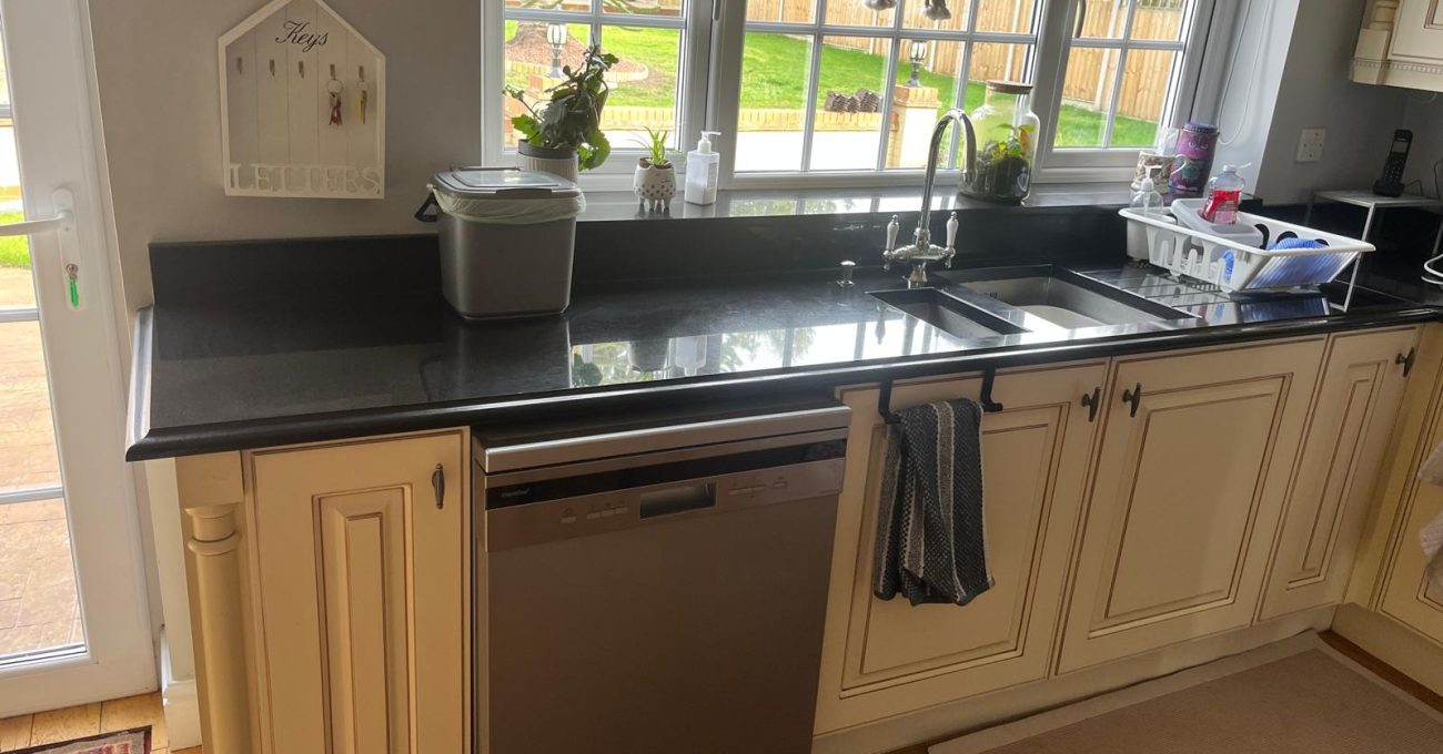 Dated cream raised-panel kitchen doors in Yateley, Hampshire before replacement, with the black granite worktops that were kept