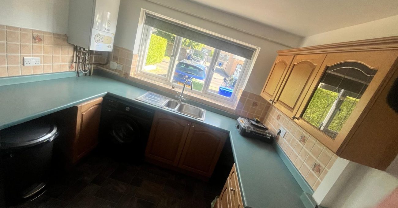Dull, dated kitchen in Farnborough, Hampshire before replacement, with green worktops, floral wall tiles and a wall-mounted boiler