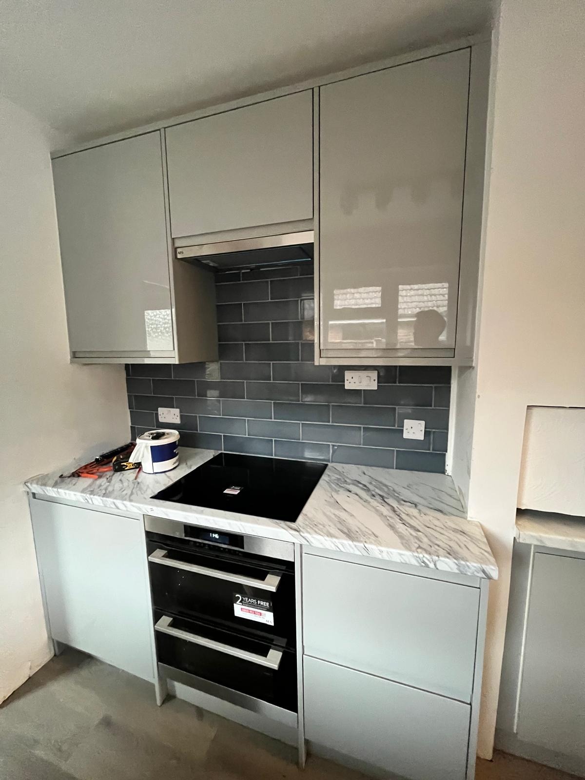 Completed Portofino kitchen in Guildford, Surrey with gloss painted units, teal metro splashback and integrated oven